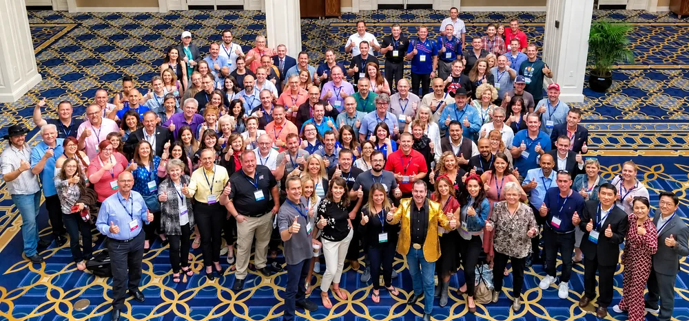 A large group of seminar attendees giving a thumbs-up in a hotel ballroom