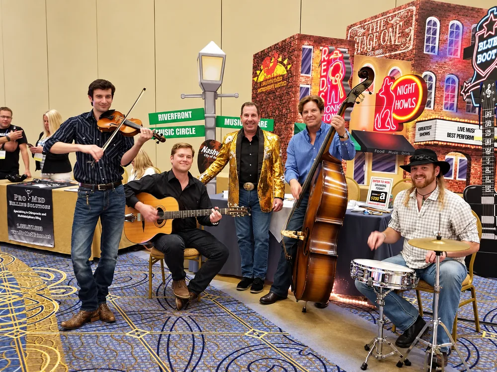 Dr. Mark Sanna in a gold jacket with a country band at an exhibit booth