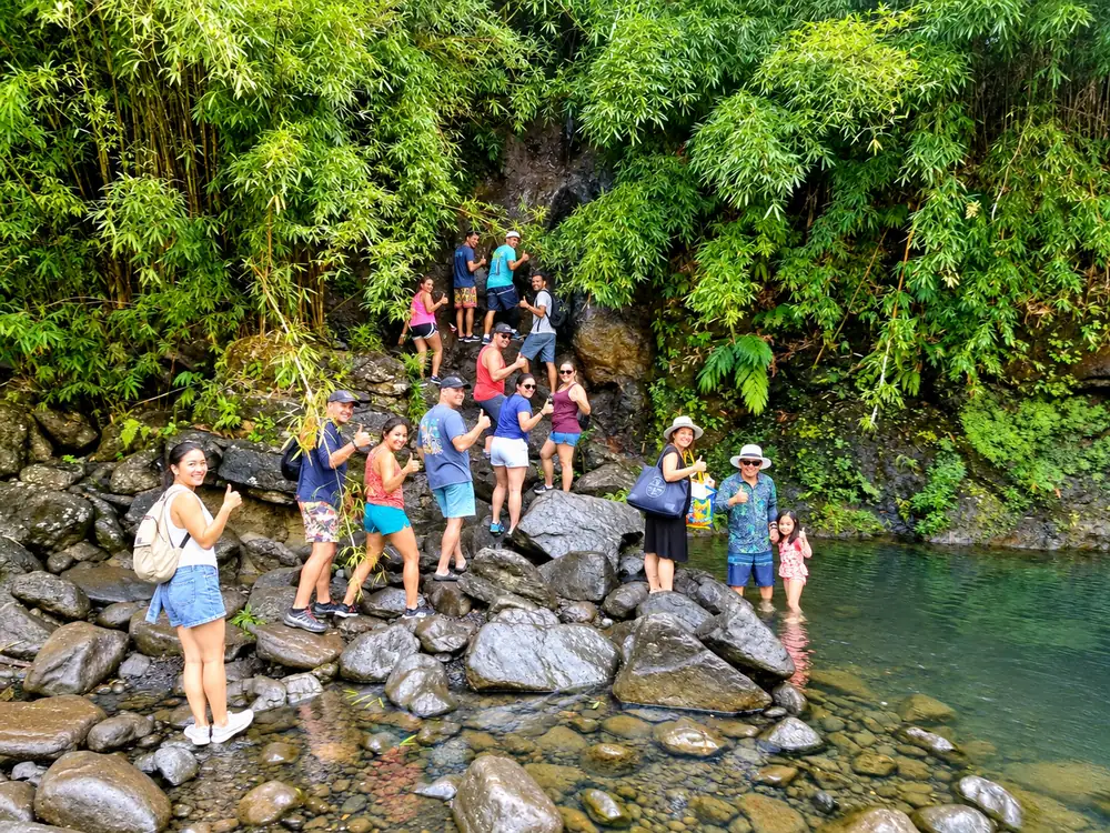 A group hiking over rocks beside a jungle waterfall pool